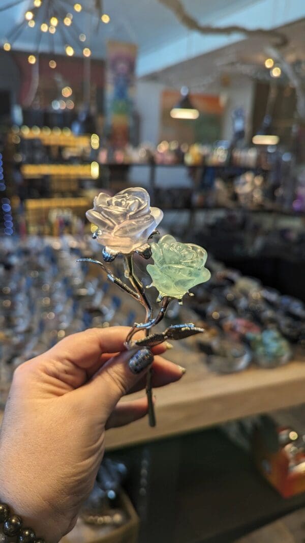 A person holding a glass rose in front of a store window.