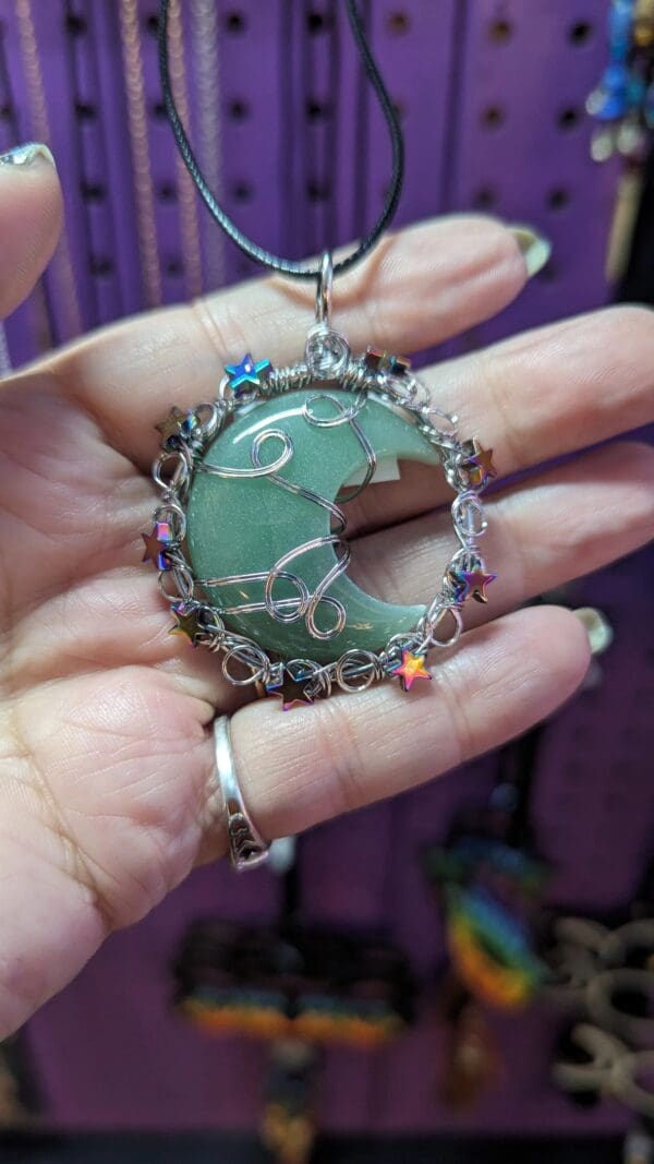 A person holding up a green moon necklace.