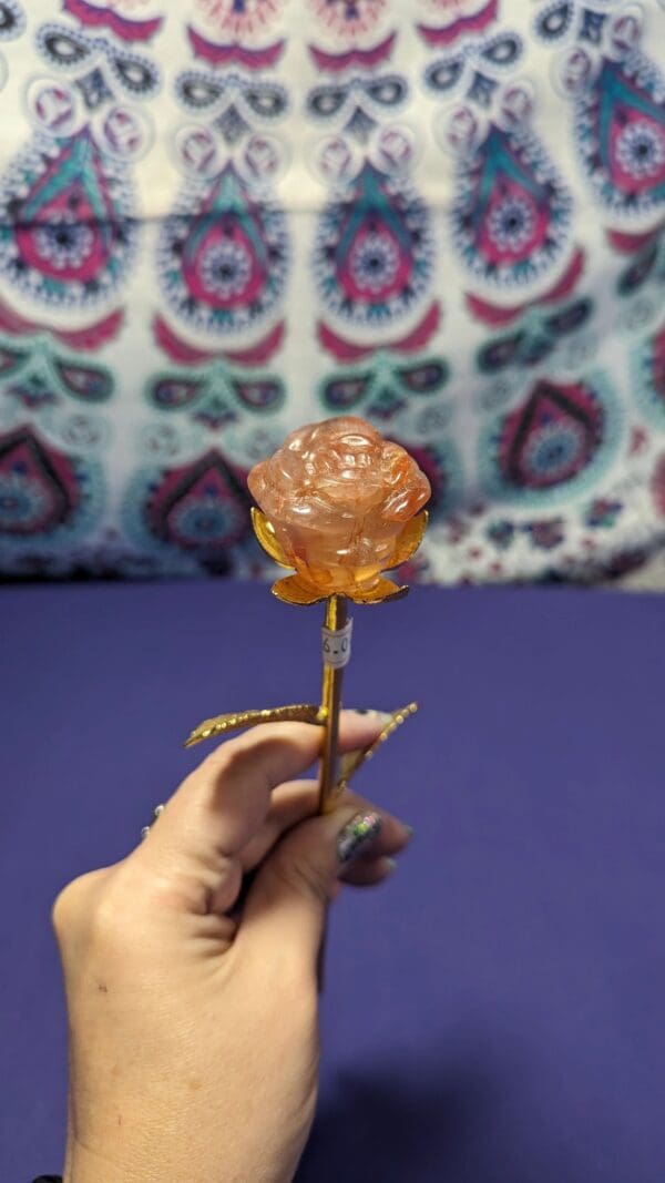 A person holding an orange rose shaped lollipop.