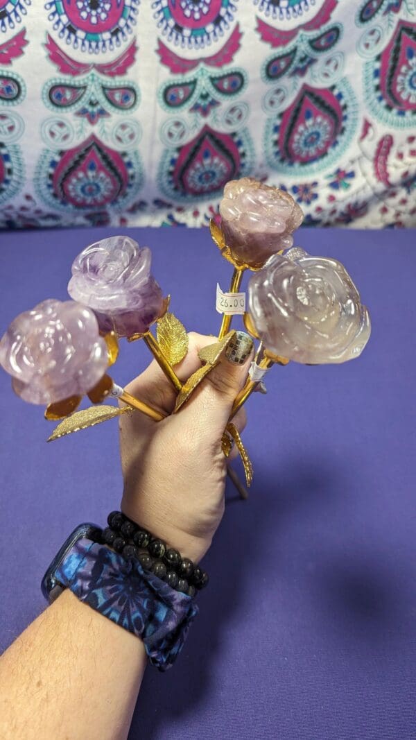 A hand holding three roses with purple stems.