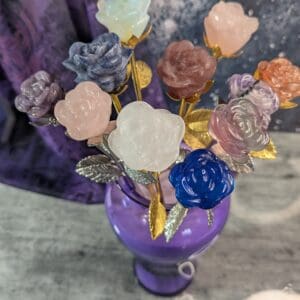 A vibrant purple vase holding colorful artificial flowers with golden stems.