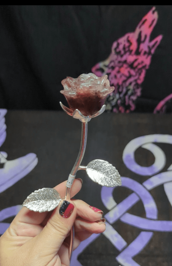 A hand holding a metal rose with leaves.