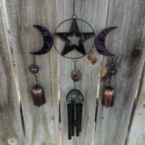 A wind chime with stars and moons hanging on the side of a wooden fence.