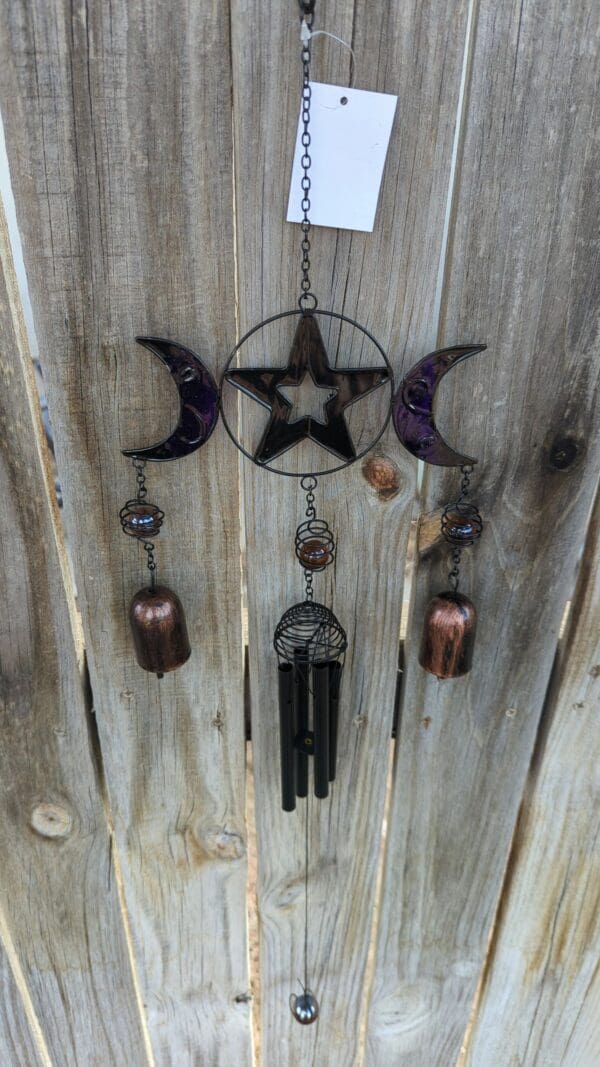 A wind chime with stars and moons hanging on the side of a wooden fence.