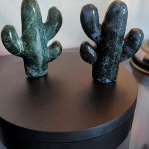 Two green cactus figurines sitting on top of a black box.