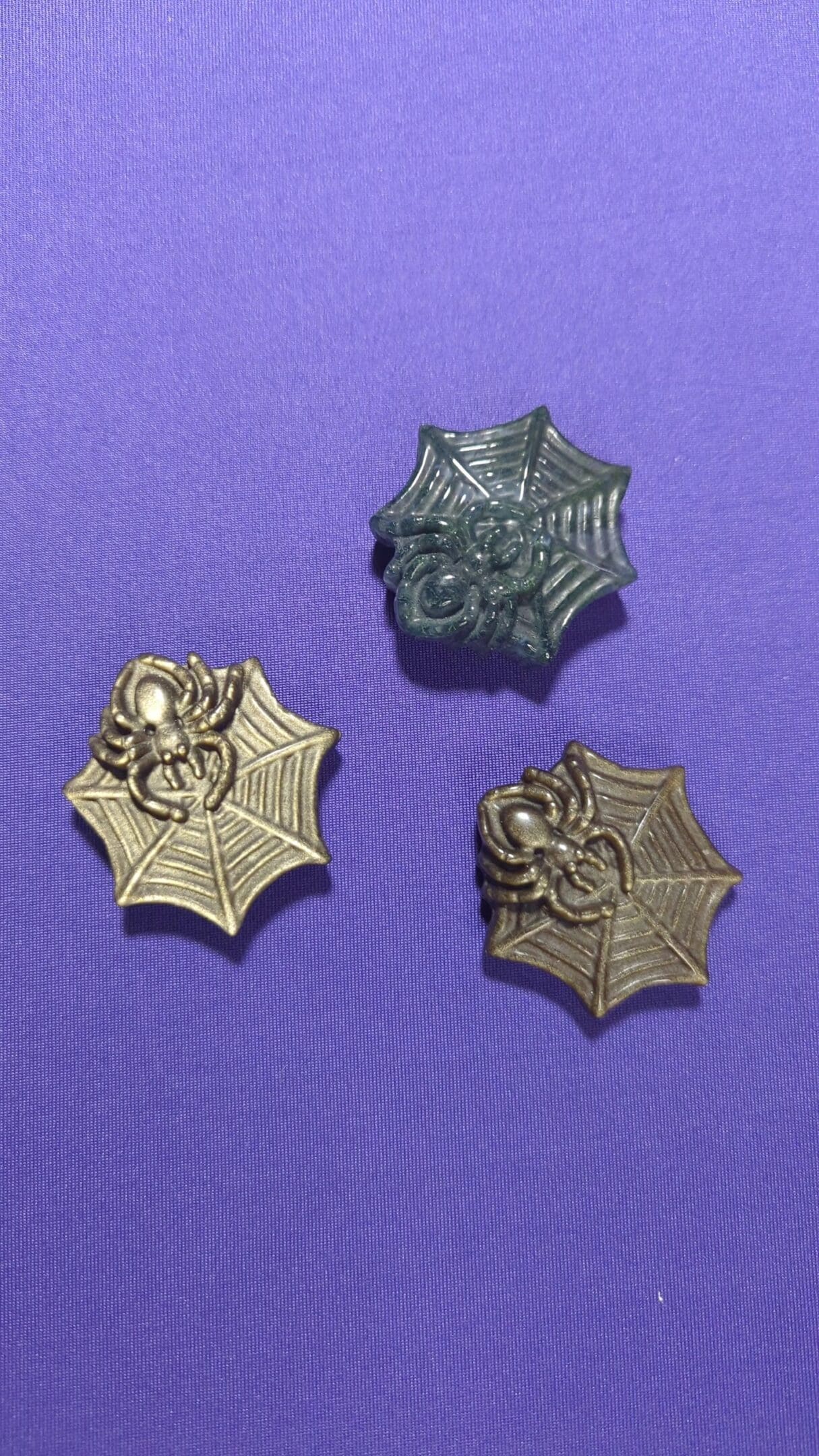 A group of three spider-man pins on purple background.