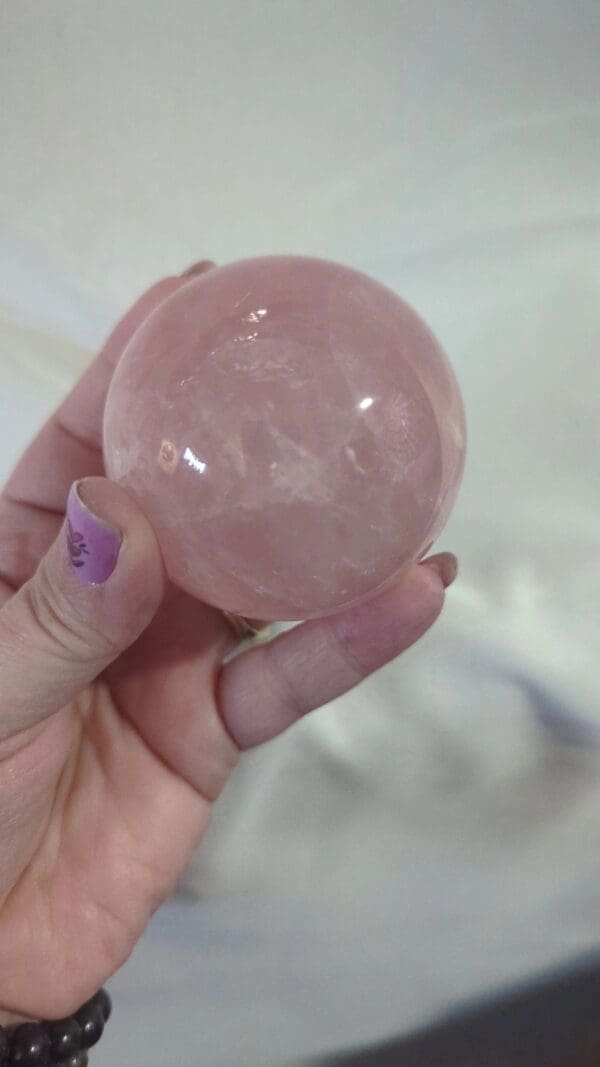 A person holding a pink ball of crystal