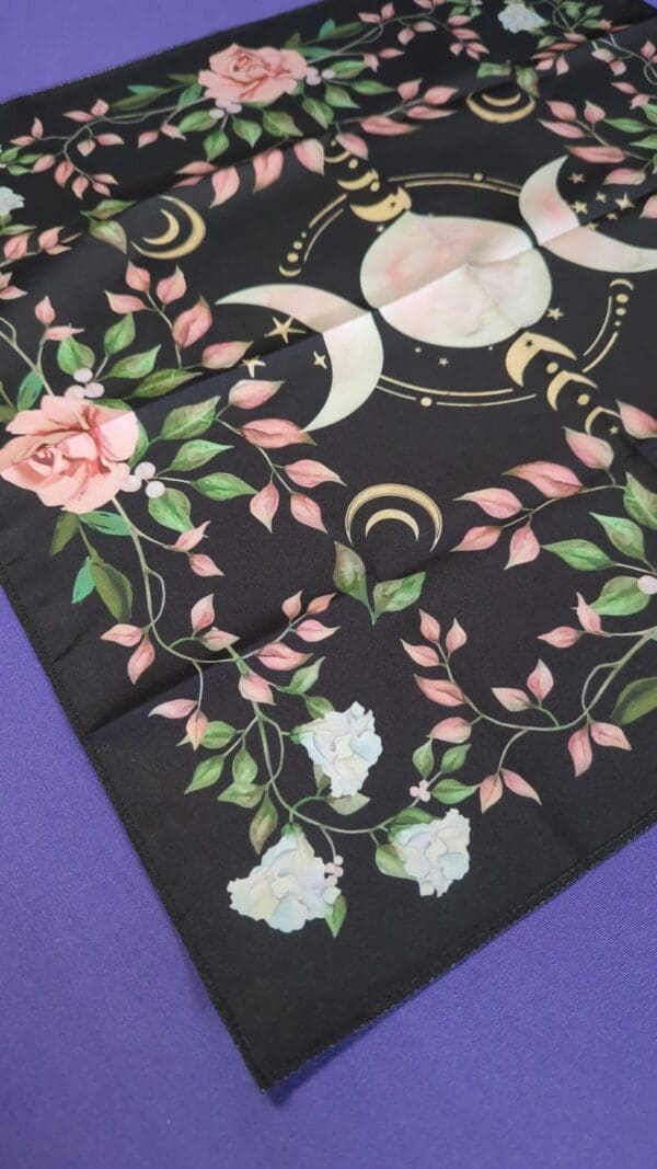 A close up of the back of a black scarf with flowers and moons