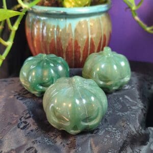 Three green pumpkins sitting on a rock near a plant.