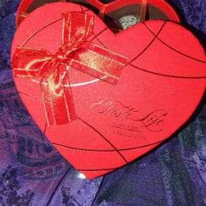 A red heart shaped box with a bow on top of it.