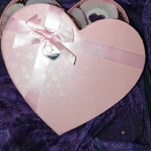 A pink heart shaped box with a bow on top of it.