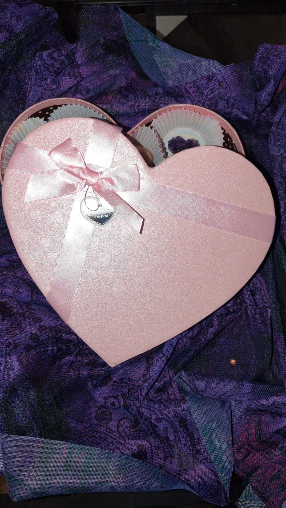 A pink heart shaped box with a bow on top of it.