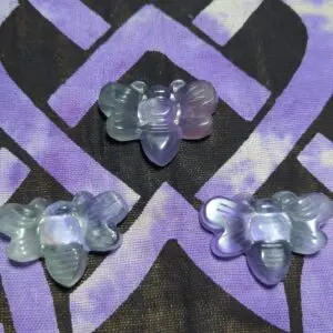 Three purple and white butterfly shaped beads on a patterned background.