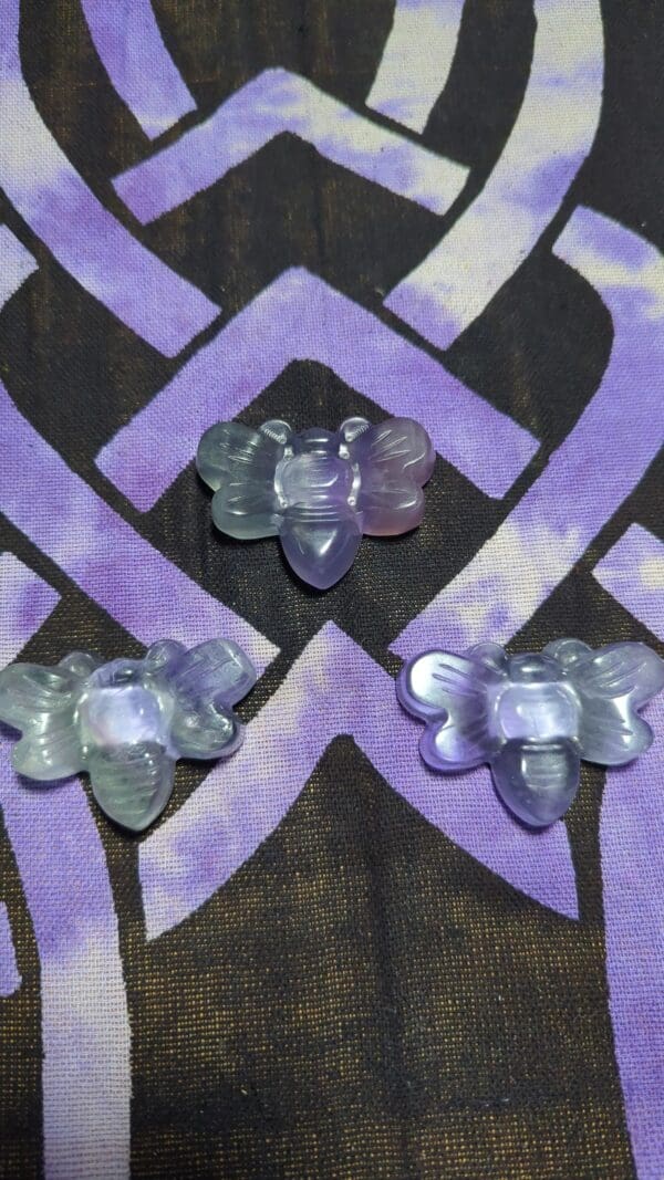 Three purple and white butterfly shaped beads on a patterned background.